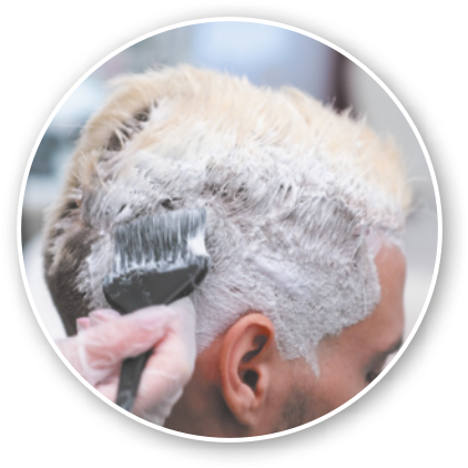 Fotografia de mão manuseando um pincel sobre o cabelo de uma pessoa. O cabelo está coberto por substância cremosa.