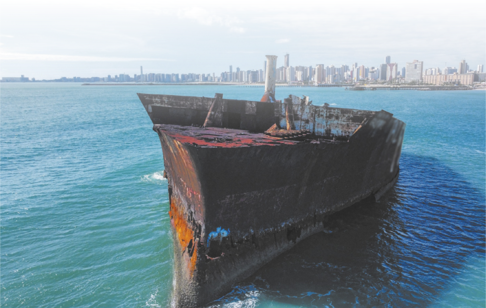 Fotografia de um navio no mar. Sua estrutura está danificada e coberta por ferrugem.