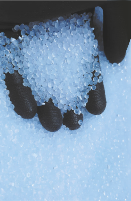 Fotografia de mão com luva pegando uma porção de pellets, que são grãos plásticos.