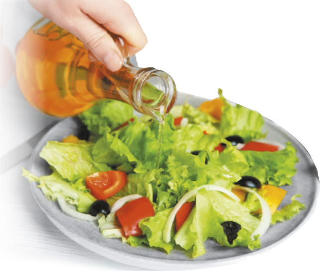 Fotografia de mão segurando um frasco, vertendo vinagre sobre uma travessa de salada.