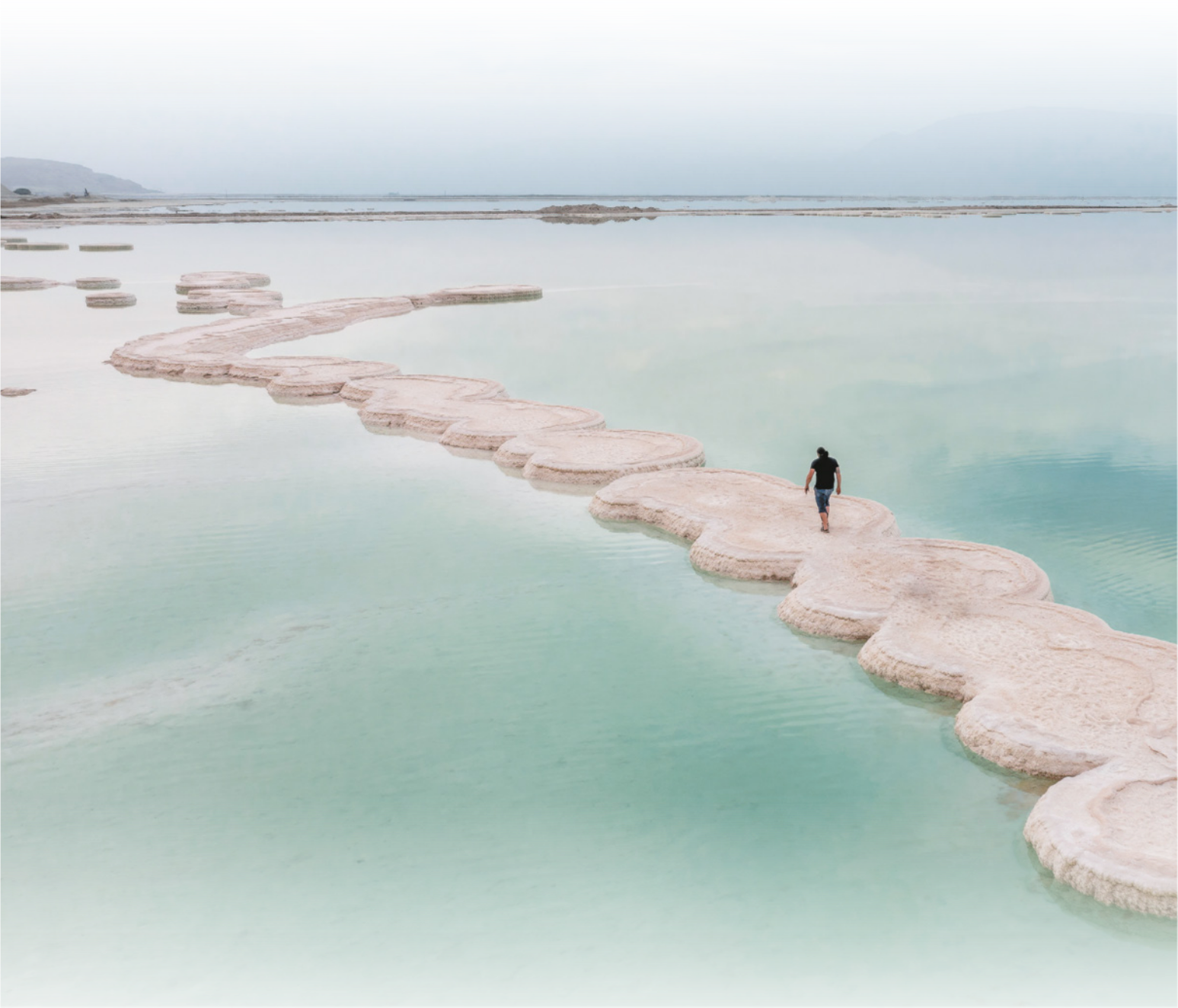 Fotografia com vista de cima de uma pessoa caminhando em ilhotas brancas em meio à água do mar.