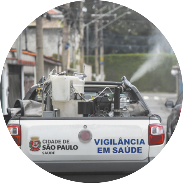 Fotografia de um automóvel carregando um equipamento na carroceria. O equipamento está pulverizando algo no ambiente.