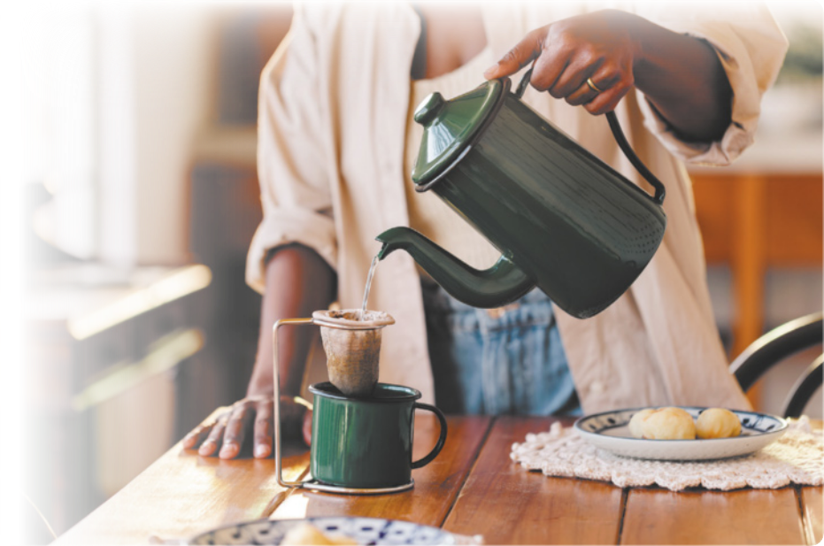 Fotografia de uma pessoa despejando água de uma chaleira sobre um coador com café. O coador está sobre uma xícara.