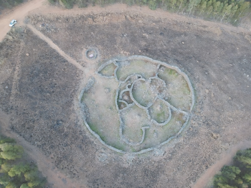 Fotografia aérea de uma grande escultura de linhas rochosas configurando um desenho circular com formas curvas internas, dividindo o espaço interno do círculo em setores de formatos irregulares.