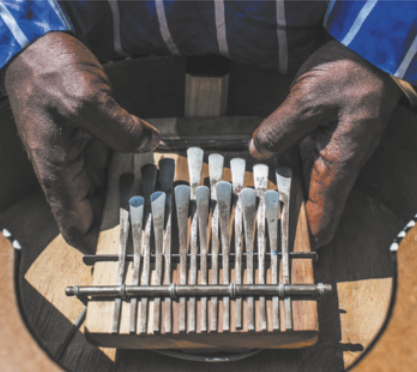 Fotografia de mãos de um músico segurando uma kalimba: um instrumento com pequenas hastes de metal instaladas sobre uma caixa acústica de madeira.