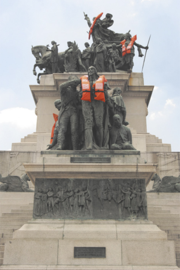 Fotografia de um monumento com esculturas representando personagens e figuras históricas sobre pedestais, algumas delas estão usando coletes salva-vidas.