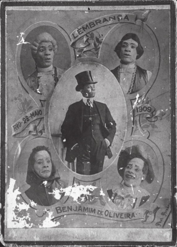 Reprodução de painel com cinco retratos fotográficos em preto e branco de Benjamim de Oliveira. Ao centro, ele está em pé, de terno e colete, usando uma cartola, com as mãos nos bolsos. No canto superior esquerdo, ele está vestido com uma peruca grisalha e cacheada; no canto superior direito, ele está com uma peruca de cabelos lisos pretos, vestido com um colete; no canto inferior esquerdo, ele está com um capuz e o rosto pintado de branco; e no canto inferior direito, ele está vestido como palhaço, com um chapéu. Faixas decorativas no painel contém as palavras 'Lembrança. Rio. 28 de maio de 1909. Benjamim de Oliveira'.