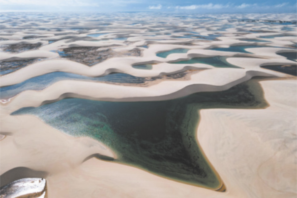 Fotografia aérea de uma paisagem desértica com trechos de dunas de areia em meio a muitas áreas alagadas.