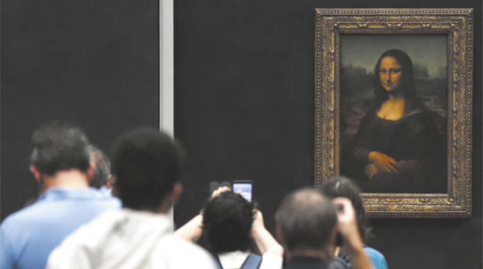 Fotografia de pessoas em um espaço expositivo diante da pintura da Mona Lisa, que representa uma mulher de vestido com uma mão apoiada sobre a outra, com uma paisagem ao fundo. As pessoas estão longe do quadro, fotografando-o com seus smartphones.