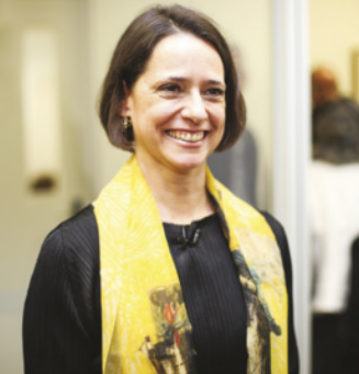Fotografia de Inês Bogéa. Ela é uma mulher branca, com cabelos lisos e curtos, na altura do queixo. Ela está sorrindo e usa um lenço no pescoço.