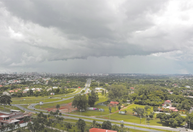 Fotografia de um local urbano com o céu com coloração acinzentada e muitas nuvens. Abaixo, há construções, ruas e vegetação.