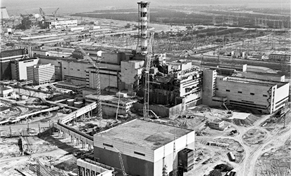 Fotografia aérea em preto e branco de uma usina nuclear com diversos prédios e instalações. No centro há uma torre alta.