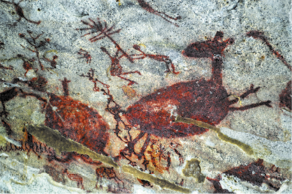 Fotografia de uma pintura rupestre com silhuetas de animais quadrúpedes e de pessoas segurando estruturas semelhantes a galhos com folhas.