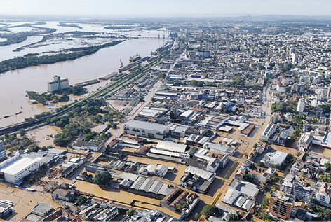 Fotografia da vista aérea de uma cidade completamente inundada pelas águas de um grande rio que se encontra do lado esquerdo margeando a cidade.