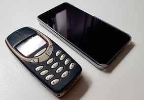 Fotografia de dois celulares; um mais antigo com um display pequeno e teclas na parte frontal e o outro mais recente com a tela touch screen.
