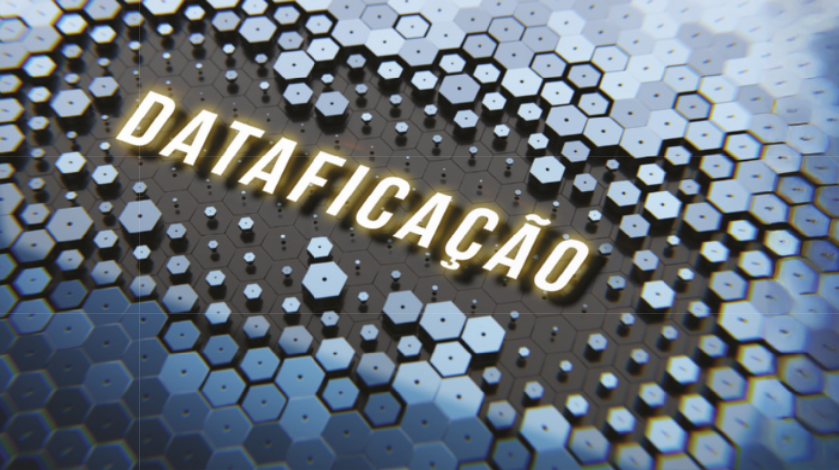 Imagem com a palavra “Dataficação' em destaque ao centro, com letras maiúsculas e iluminadas em tom amarelado. O fundo é composto por padrões de hexágonos pretos, cinzas e azuis, que lembram uma malha digital ou rede de dados.