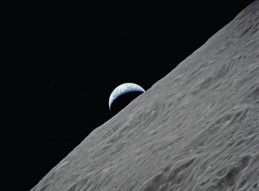 Imagem da superfície da Lua em primeiro plano, ocupando a parte inferior e inclinada diagonalmente, com textura acinzentada e repleta de relevos e crateras. Ao fundo, contra o espaço completamente negro, aparece a Terra parcialmente visível, em formato crescente e com tonalidades azuladas e brancas.