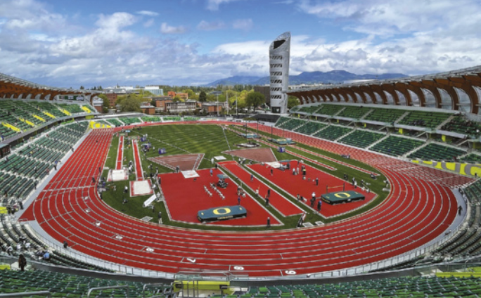 Fotografia de um estádio esportivo com arquibancadas em volta de uma pista de atletismo, com um campo de grama ao centro contendo pistas de saltos e equipamentos para outras modalidades do atletismo.
