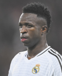 Fotografia de Vinicius Júnior. Ele é um homem com cabelos cacheados e curtos, raspados nas laterais acima das orelhas. Ele veste o uniforme do clube Real Madrid.