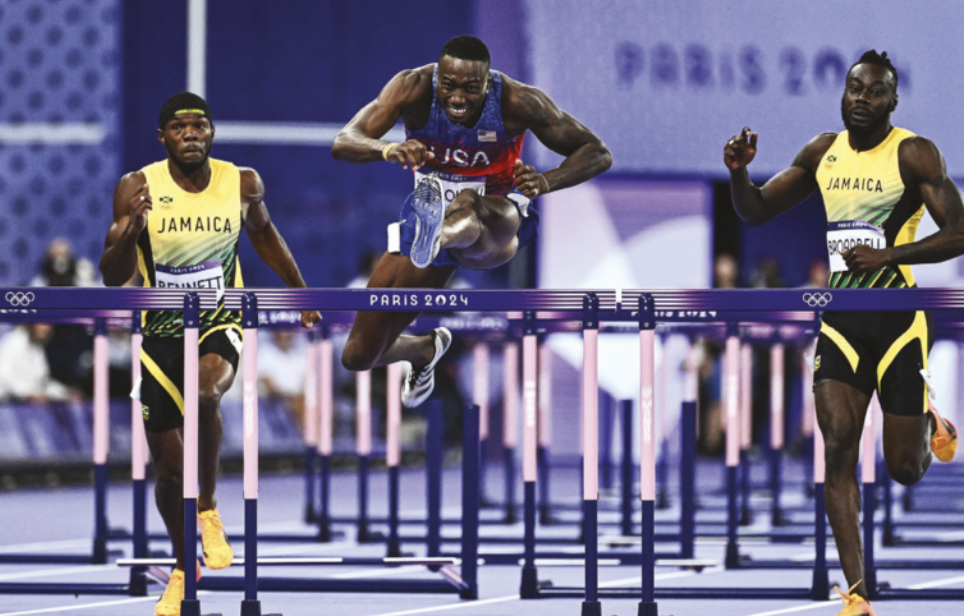 Fotografia de três corredores em uma prova de corrida em uma pista de atletismo, correndo e saltando sobre obstáculos.