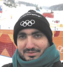 Fotografia de Gustavo de Araújo Longo. Ele é um homem com barba, usando cachecol e um gorro, com uma paisagem nevada ao fundo.