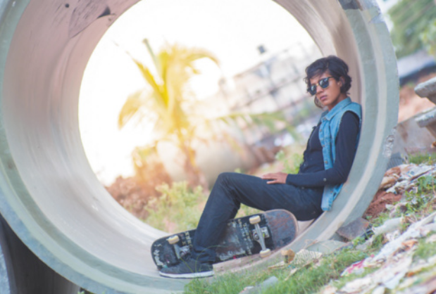 Fotografia de Atita Verghese. Ela é uma mulher de cabelos curtos, usando óculos escuros e um colete, sentada no interior de um grande cilindro de concreto, com um skate entre as pernas.