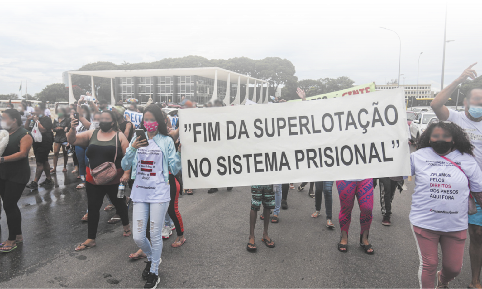 Imagem de manifestantes caminhando próximo ao Palácio do Planalto. Entre eles, duas mulheres carregam uma faixa com a seguinte frase: Fim da superlotação no sistema prisional.