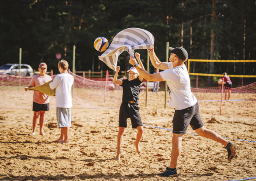 Imagem de pessoas jogando vôlei em uma quadra de areia. Elas estão em duplas e utilizam uma faixa de tecido para arremessar a bola.