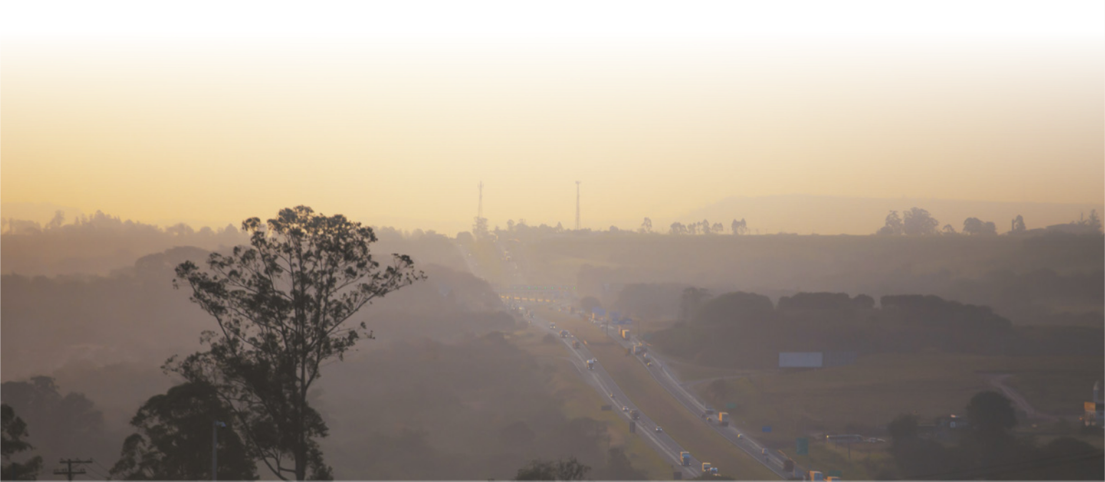 Imagem de rodovia em uma região serrana, com vegetação esparsa. A paisagem está parcialmente encoberta.