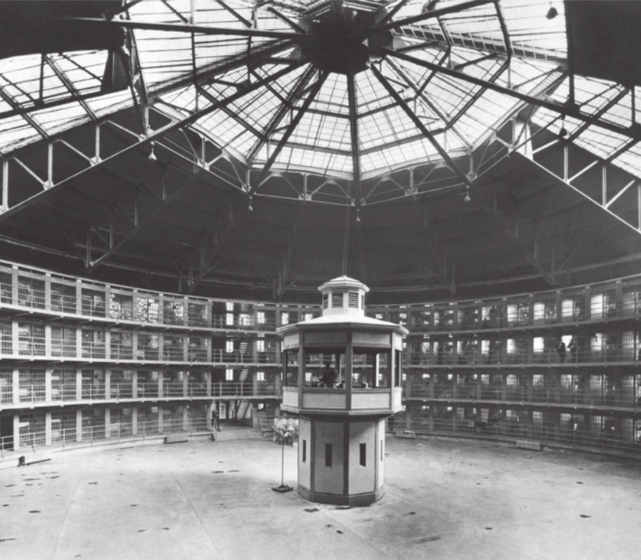 Imagem em preto e branco de uma prisão. As celas situam-se em uma construção de quatro níveis, ao redor de uma área circular com uma torre central.