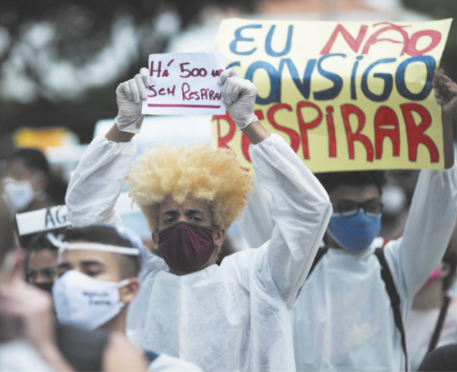 Imagem de manifestantes com máscaras e roupas de proteção. Dois deles seguram cartazes com as seguintes frases: eu não consigo respirar. Há 500 anos sem respirar.