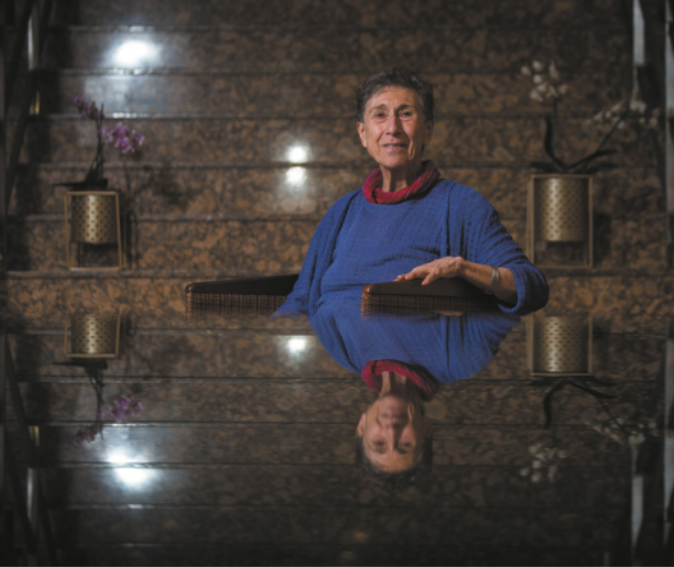 Fotografia de Silvia Federici. Ela é branca, idosa, possui cabelo curto, usa blusa com gola colorida e está sentada diante de uma mesa.