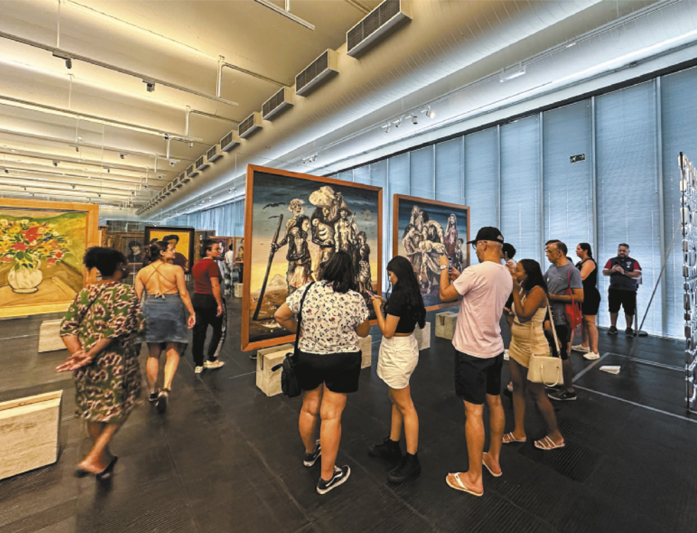 Imagem de pessoas em um museu. Quadros estão fixados em suportes retangulares, com a frente e o verso expostos aos visitantes.