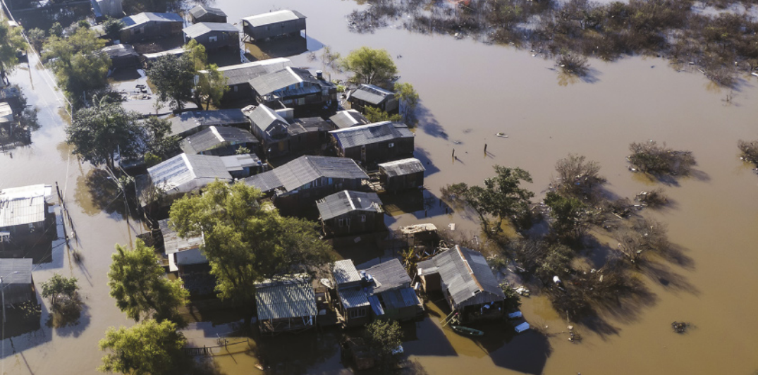 Imagem aérea de bairro alagado. O bairro contém casas, que estão parcialmente submersas, e vegetação.