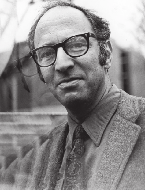 Fotografia em preto e branco de Thomas Kuhn. Ele é branco, calvo e usa óculos, camisa, gravata e paletó.