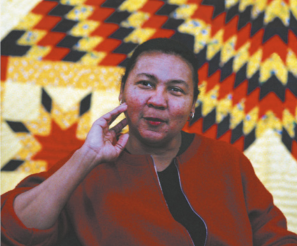Imagem de bell hooks. Ela é negra, está com o cabelo preso, o rosto apoiado sobre a mão direita e usa casaco com zíper.