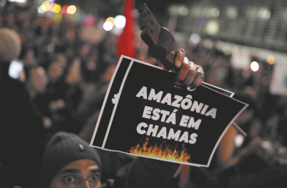 Imagem de multidão em um protesto. Um dos manifestantes segura cartazes e uma ferramenta.
