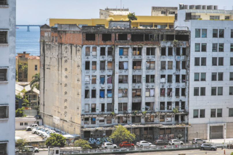 Imagem de edifício com oito pavimentos e diversas janelas quebradas, cobertas com cortinas ou tapumes.