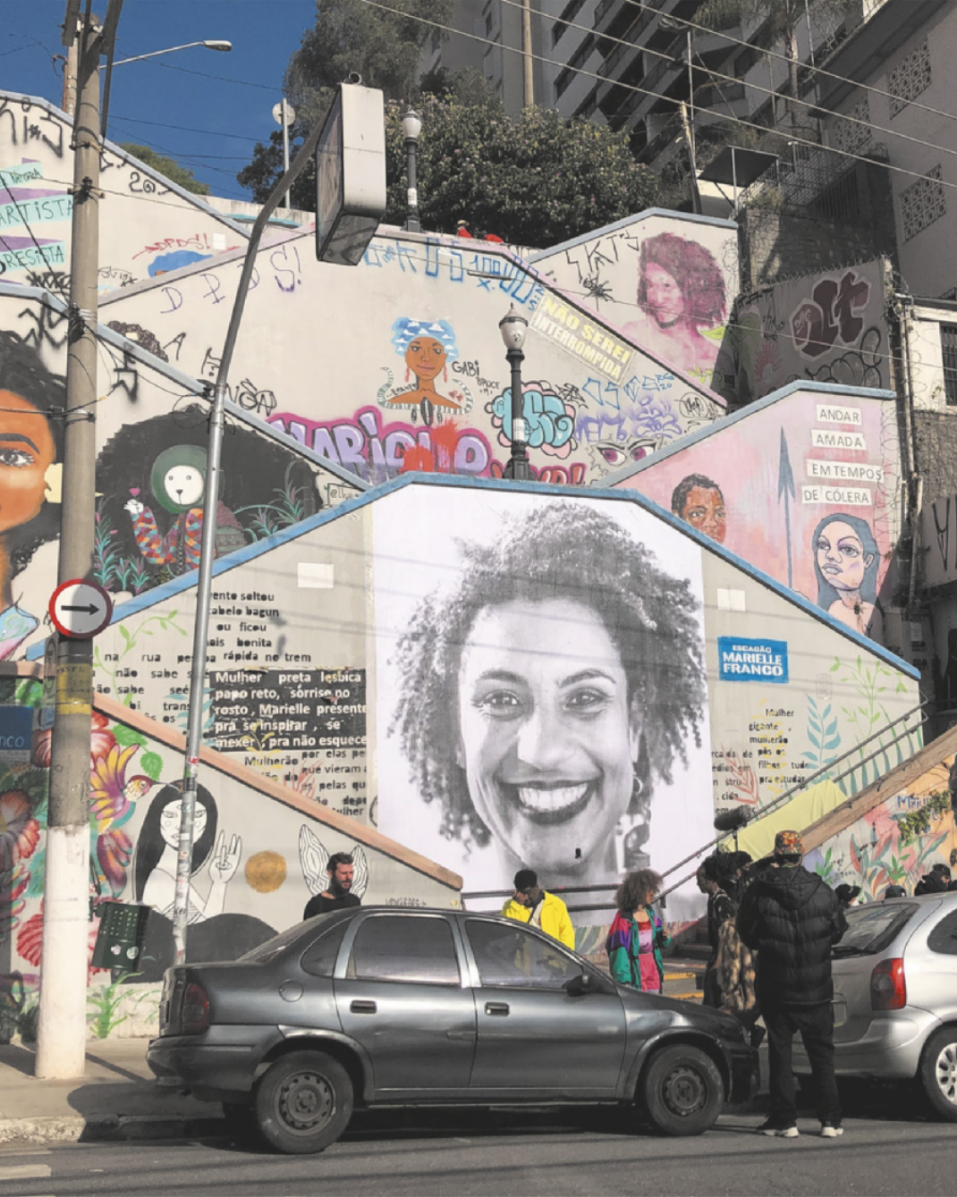 Imagem de pinturas e grafites nas laterais de uma escadaria. Uma das pinturas retrata Marielle Franco sorrindo.
