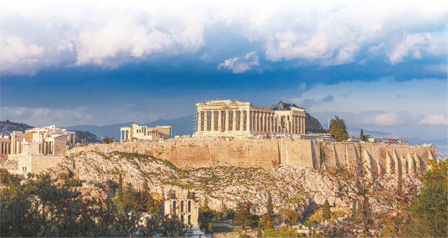 Imagem da acrópole de Atenas. No topo, encontram-se as ruínas de um templo retangular, com diversas colunas.