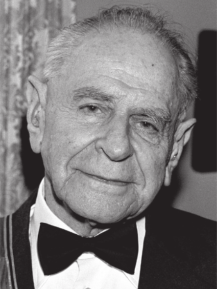 Fotografia em preto e branco de Karl Popper. Ele é idoso, calvo, usa terno e gravata borboleta e está sorrindo.