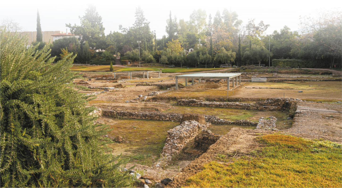 Imagem de ruínas em uma área plana. As bases das paredes delimitam construções de planta quadrangular e algumas delas estão protegidas por uma cobertura.