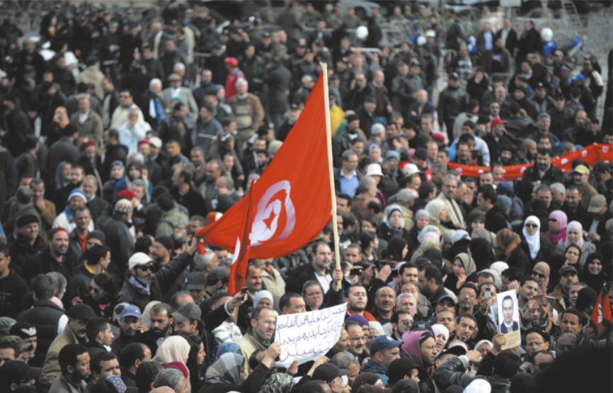 Imagem de multidão em uma manifestação. Uma pessoa, ao centro, carrega a bandeira da Turquia.