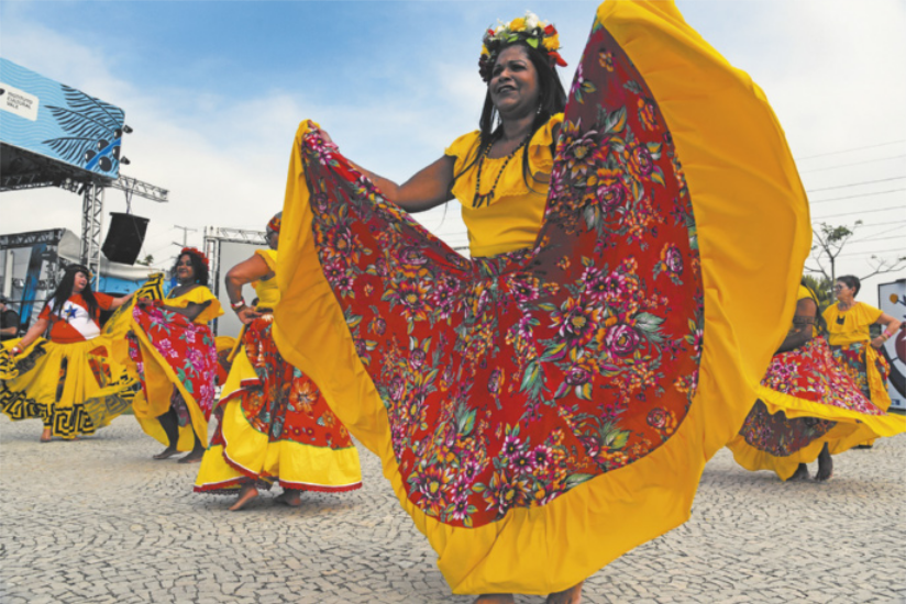 Imagem de mulheres dançando carimbó. Elas usam saia rodada florida, blusa com babados e adorno floral na cabeça.