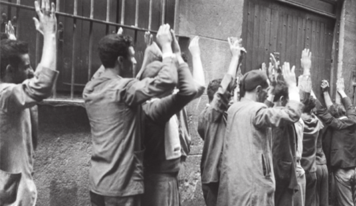 Imagem em preto e branco de pessoas enfileiradas, com as mãos erguidas.