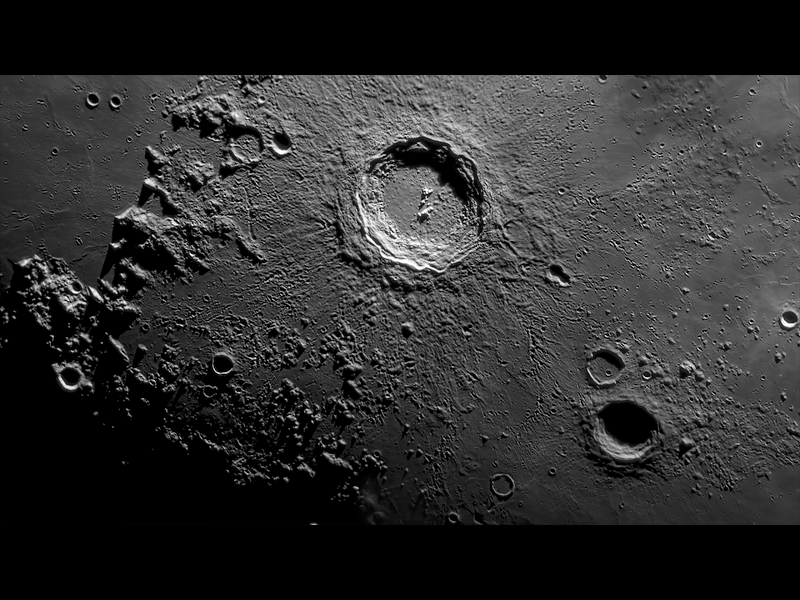 Fotografia em preto e branco evidenciando a cratera lunar denominada Copérnico. A cratera tem formato circular e se destaca entre as demais que estão próximas por ser a maior entre elas.