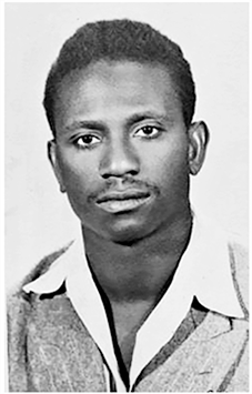 Fotografia em preto e branco de um homem negro com cabelo enrolado e curto, usando camisa com gola branca.