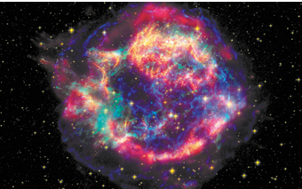 Fotografia do espaço com uma formação colorida, circular irregular em meio a várias estrelas. A formação tem cores brilhantes incluindo vermelho, amarelo e azul. Ao fundo há muitos pontos brilhantes e amarelos, as estrelas.