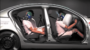 Fotografia de uma simulação de colisão de um carro com ativação do airbag. O carro é visto a partir da lateral, sem as portas e possui bonecos sentados, que simulam pessoas. Na frente, no banco do passageiro o airbag está ativado, e o boneco está inclinado sobre o airbag. No banco traseiro, os bonecos estão sentados, com o corpo um pouco à frente do encosto do banco.