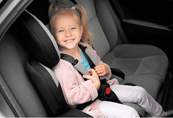 Fotografia de uma menina sorrindo sentada em uma cadeirinha no banco de trás de um carro, usando cinto de segurança.